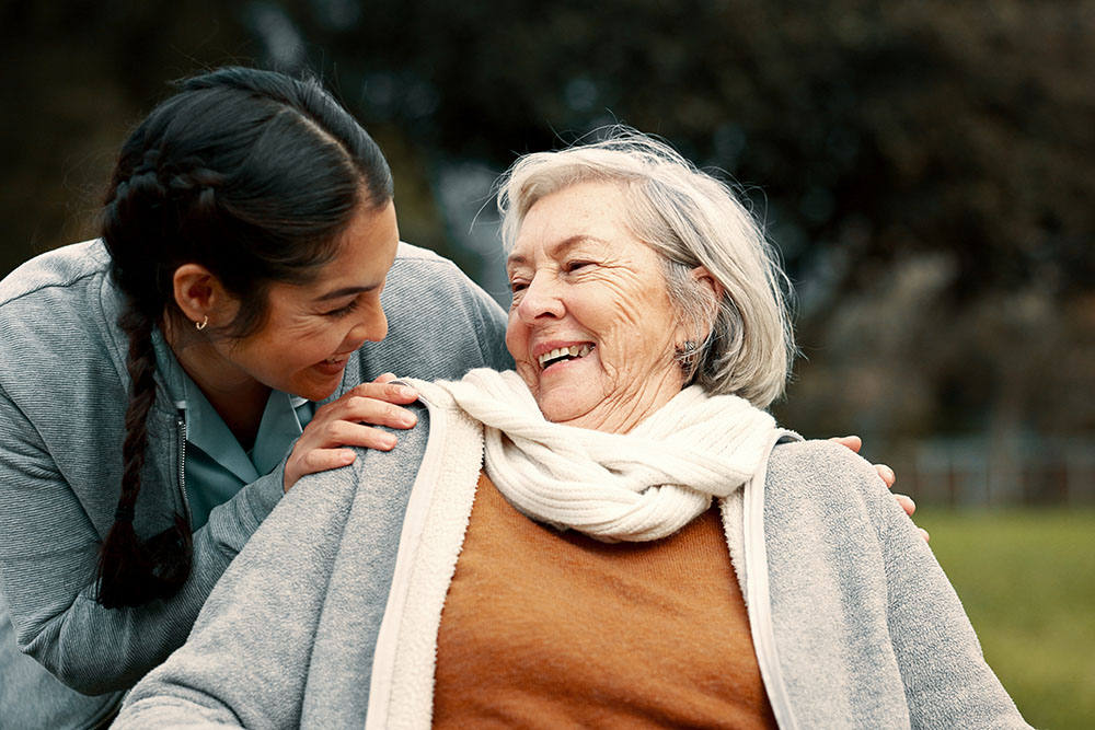 Caregiver helping woman with disability in park for support, trust and care in retirement. Nurse talking to happy senior patient in wheelchair for rehabilitation, therapy and conversation in garden